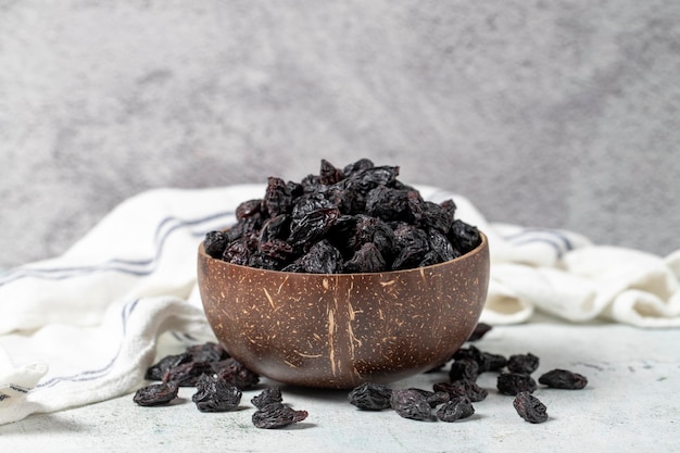 Dried black grapes on stone background Dried grapes in coconut bowl Nuts varieties Healthy eating close up