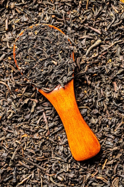 Dried black tea leaves in wooden spoon Top view