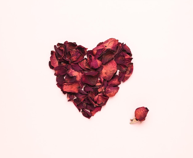 A dried bouquet of roses and a heart of rose petals on a pink background The concept of a romantic relationship Flat lay