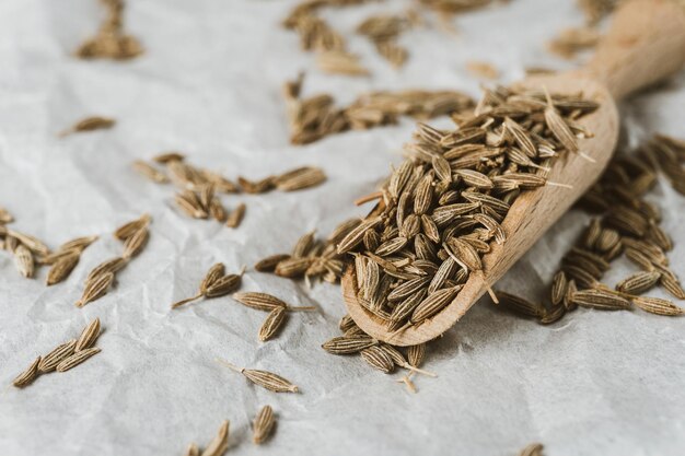 dried caraway cumin seeds in wooden spoon and pile of zira nearby on white crumpled paper closeup