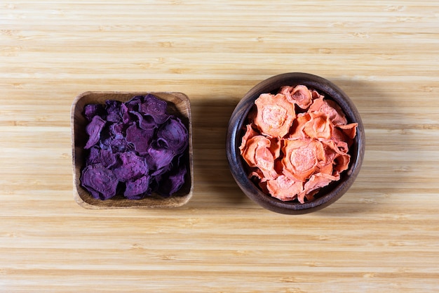 Dried carrot and beet chips in a wooden bowl on a cutting Board.