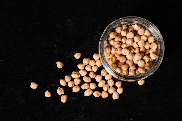 Dried chickpeas in a glass jar on a black surface. top view, space for writing.