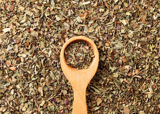 Dried chopped basil in a wooden spoon close-up on a background of seasoning. The view from top