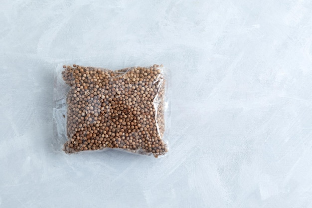 Dried coriander seeds in clear plastic bag on grey textured background Top view copy space