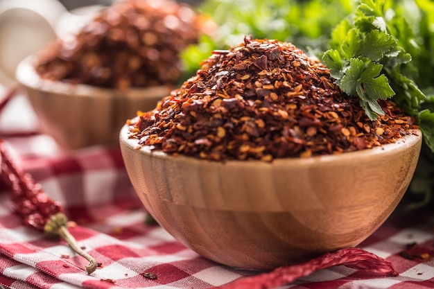 Dried and crushed chili peppers in wooden bowles with parsley herbs.