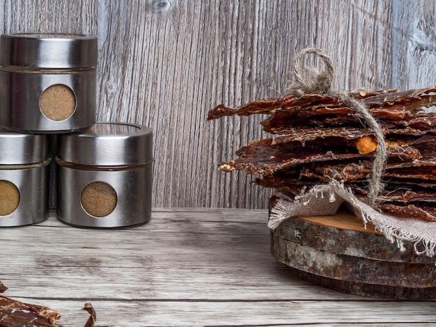 Dried or dehydrated meat slices with spices in jars on wooden background copy space