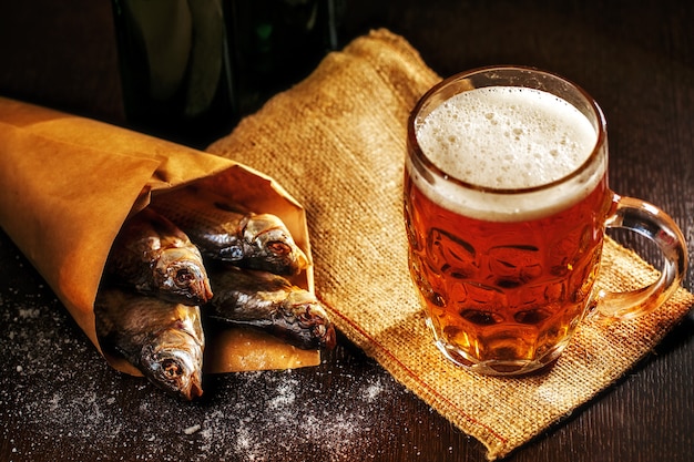 Dried fish and vintage glass of beer on dark wooden table