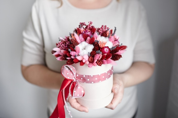 Dried flower bouquet with grasses in pink round hat box in hands