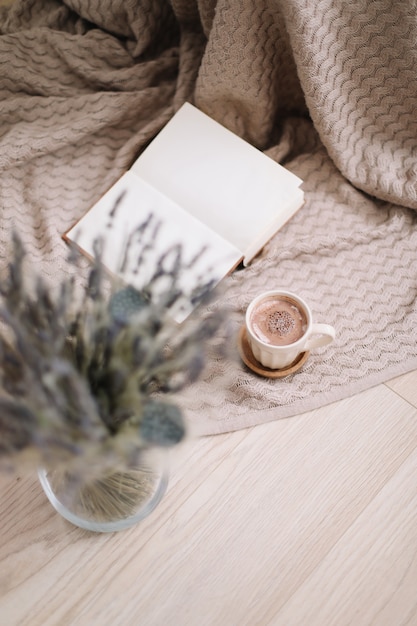 Dried flowers and a cup of cappuccino with book on wooden background top view