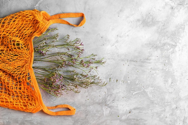 Dried flowers in reusable shopping eco mesh bag on gray concrete background. Concept no plastic and zero waste. Copy space Top view.