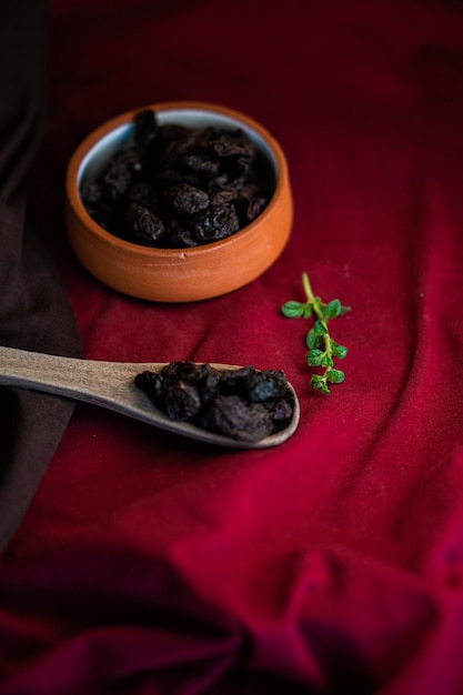 Dried fruit in a clay pot and wooden spoon on cherry fabric