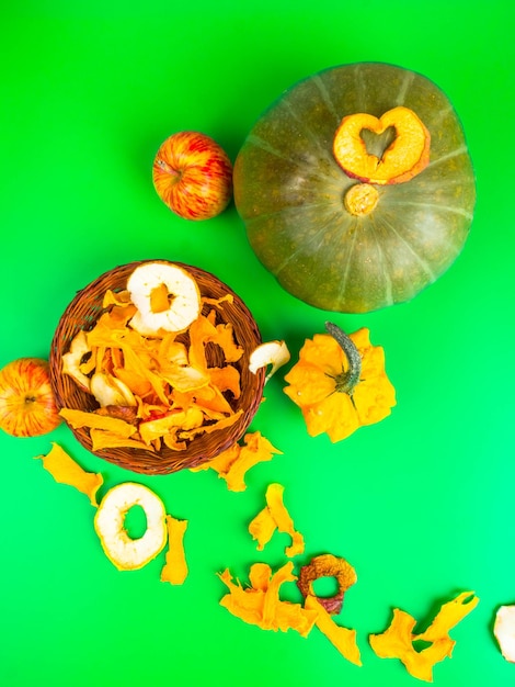 Фото Сушеные фрукты и овощи нарезают яблочную тыкву в коричневой плетеной корзине на зеленом фоне.