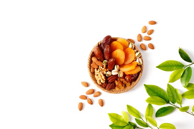 Dried fruits and nuts mixed in a wicker plate branch with young green leaves Concept of the Jewish holiday Tu Bishvat on white background with copy space