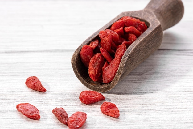 Bacche di goji secche con cucchiaio di legno su sfondo bianco