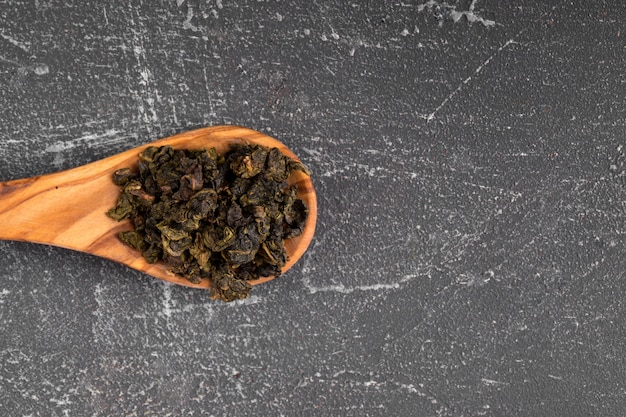 dried green tea leaves in a wooden spoon