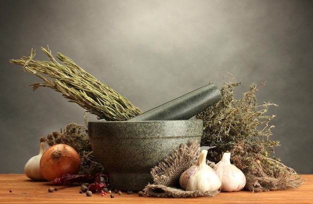 Dried herbs in mortar and vegetables on wooden table on grey background