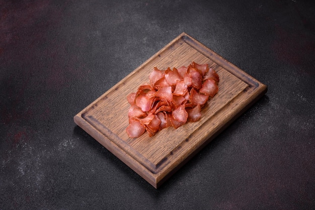 Dried meat slices with spices and herbs snacks for beer on a\
black stone background top view