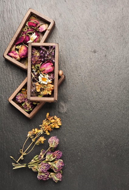 Dried medicinal herbs in wooden boxes for herbal healing tea top view on a black slate background