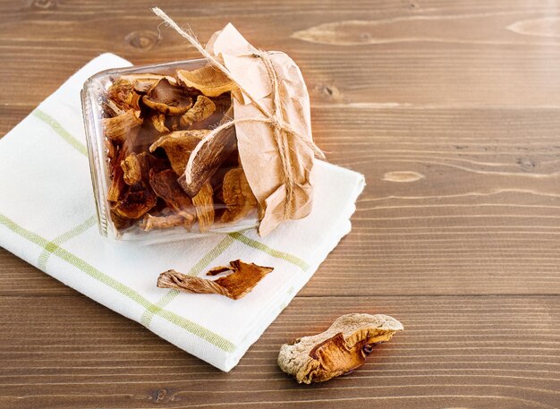 Dried mushrooms in a glass jar covered with paper on a wooden table Organic ecofriendly food