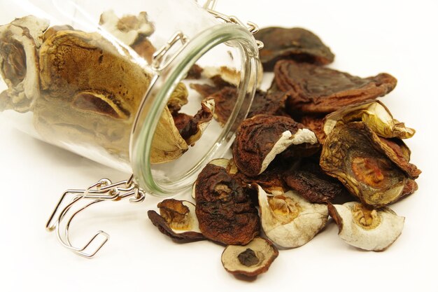 Dried mushrooms in a glass jar scattered on table