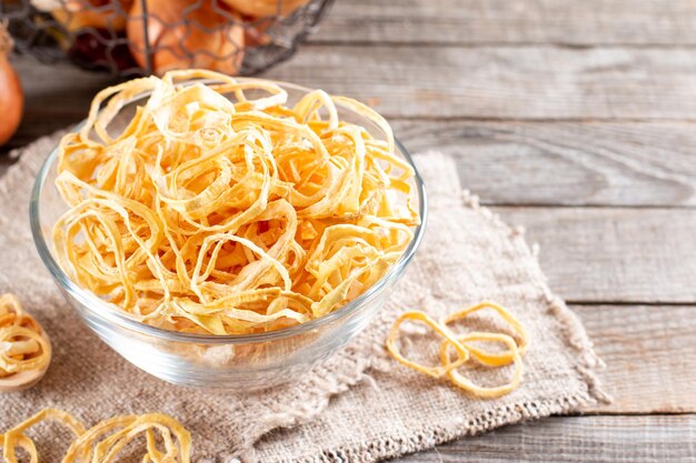 Dried onion rings in a glass bowl on a wooden table. Spices and food ingredients. Copy space