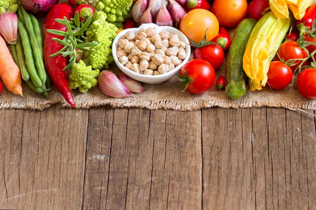 Dried organic chickpea in a bowl with raw vegetables on a wooden table close up with copy space