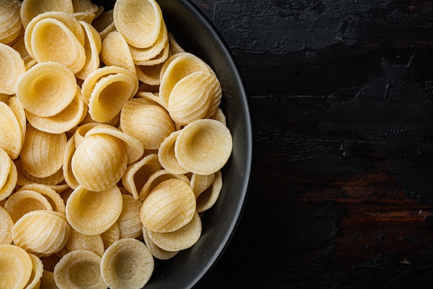 Dried pasta shells in bowl on black wooden table, flat lay