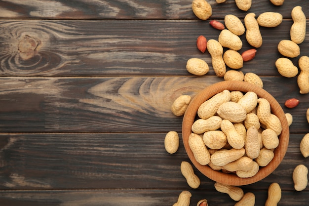 Dried peanuts in wooden bowl on brown background.