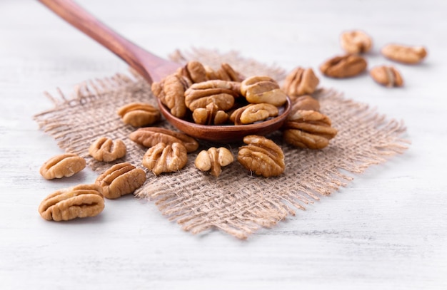 Dried Pecan Nuts in the brown wooden spoon on the piece of burlap on white Wooden Background catalog
