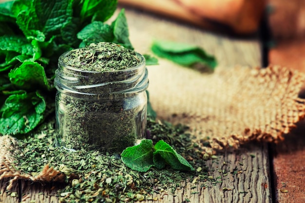 Photo dried peppermint in a glass jar and a bunch of fresh mint vintage wood background selective focus