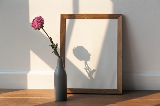 Dried pink peony flower in a gray vase by a wooden frame on the floor