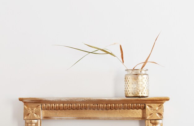 Dried plants in in golden jar on old shelf on white background