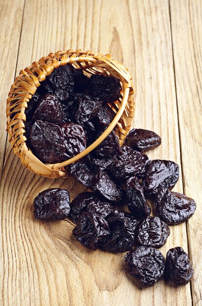 Dried plum in a basket and scattered on wooden table