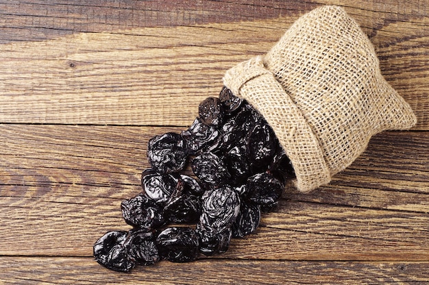 Dried plum in sack on wooden table close up