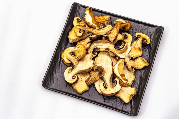 Dried porcini mushrooms isolated. Traditional ingredient for cooking healthy food. Black ceramic plate