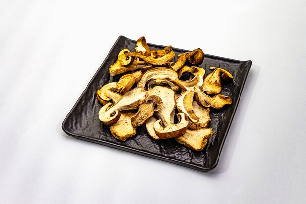 Dried porcini mushrooms isolated. Traditional ingredient for cooking healthy food. Black ceramic plate