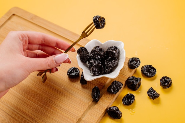 Dried prunes on a wooden board on a yellow background