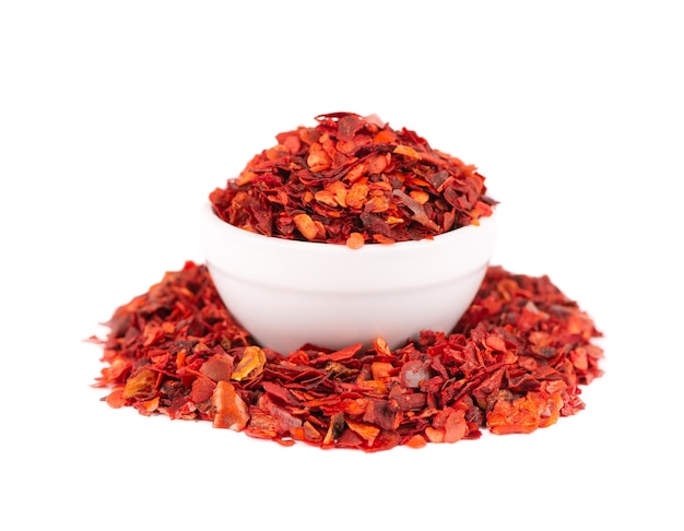 Dried red chili flakes in bowl, isolated on white background. Chopped chilli cayenne pepper. Spices and herbs.