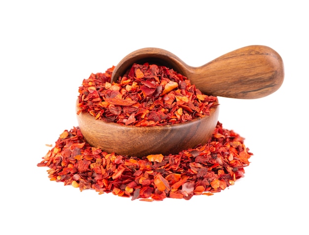 Dried red chili flakes in wooden bowl and spoon, isolated on white background. Chopped chilli cayenne pepper. Spices and herbs.