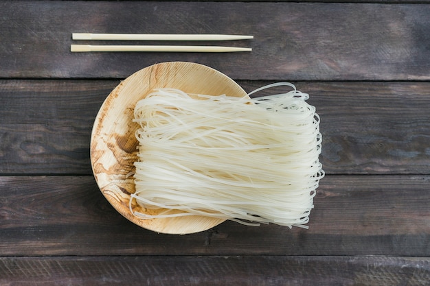 Foto vermicelli secchi del riso sul piatto con le bacchette sopra la plancia di legno