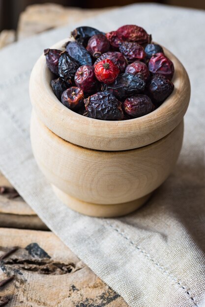 Dried rose hip berries in wood bowl, on linen towel, health concept