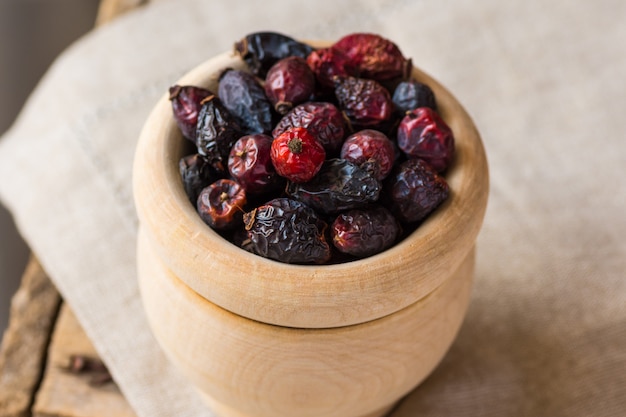 Dried rose hip berries in wood bowl, on linen towel