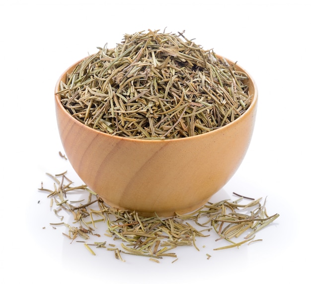 Dried rosemary leaves in wooden bowl over white background