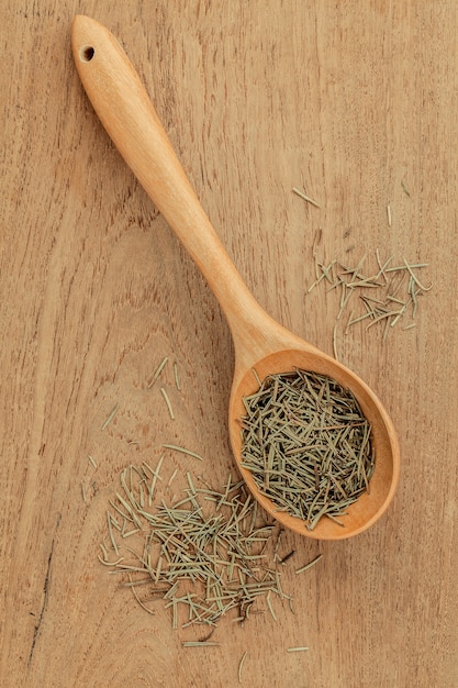 Photo dried rosemary leaves in wooden spoon on teak wood  background .