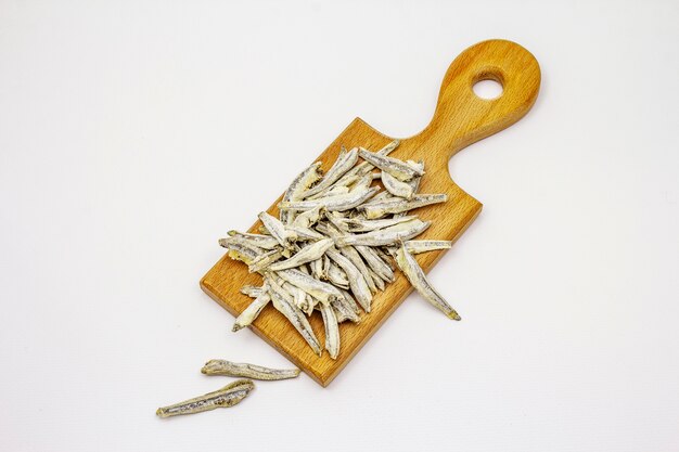 Dried salted anchovies on wooden cutting board isolated on white background