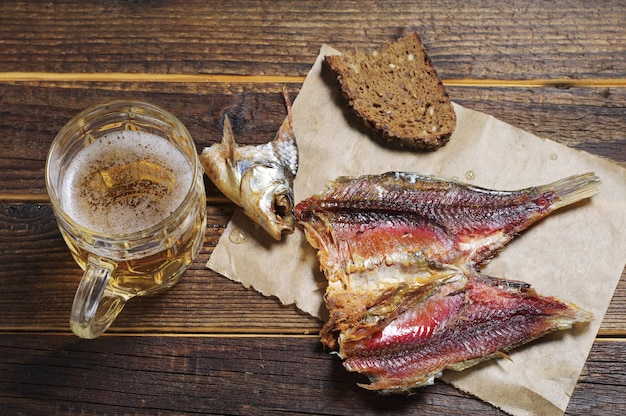 Dried salted fish and a glass of beer on wooden table