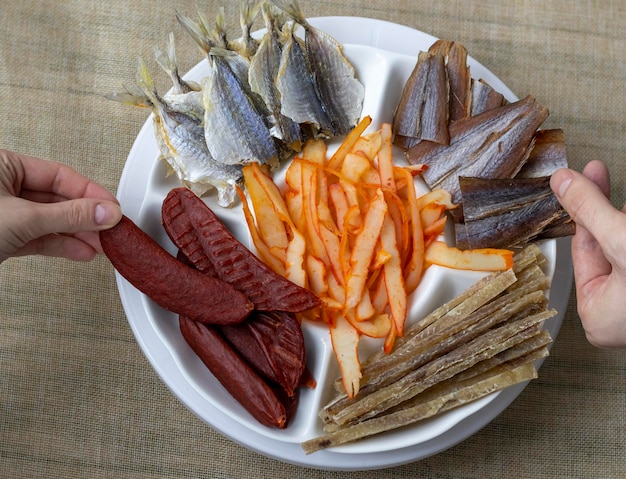 Dried Seafood Mix with Squid Mussels Tuna Yellow Minke Dried Caviar Top View Cured Dehydrated Fish Fillet as Beer Snack Nice Serving In White Round Plate Company of people take an appetizer