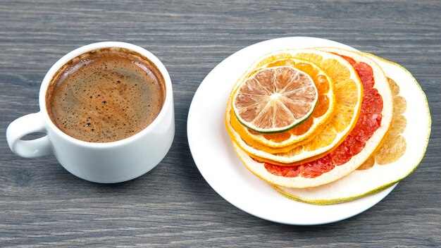 Dried slices of various citrus fruits and black coffee in a white Cup. Healthy and vitamin food