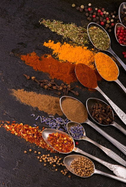 Dried spices - pepper, turmeric, paprika, anise, lavender,\
adjika, cilantro in old spoons on a black background