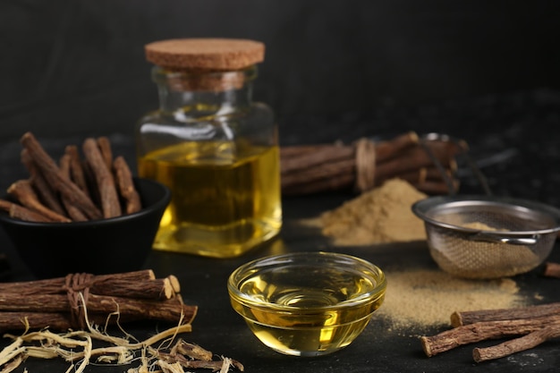 Dried sticks of licorice roots powder and essential oil on black table Space for text